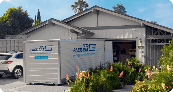 A 1-800-PACK-RAT portable storage container sits in the driveway of a home and is being filled by a customer