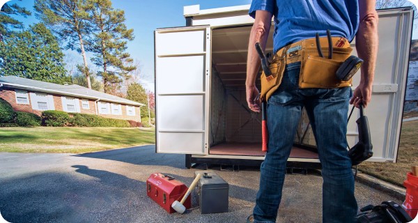 A contractor stands in front of an open 1-800-PACK-RAT portable storage container sitting on a neighborhood street