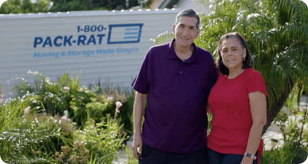 A happy couple stands in front of a 1-800-PACK-RAT portable storage container