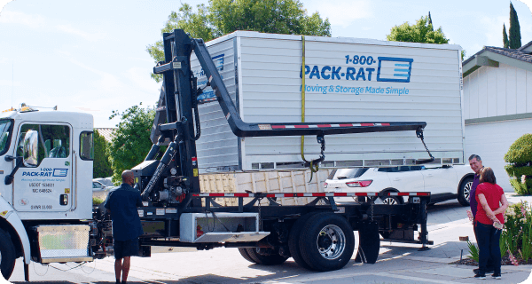 A 1-800-PACK-RAT delivery truck drops off a portable storage container to a pair of customers in their driveway