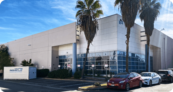 Exterior view of a warehouse facility with vehicles and 1-800-PACK-RAT portable storage container parked out front