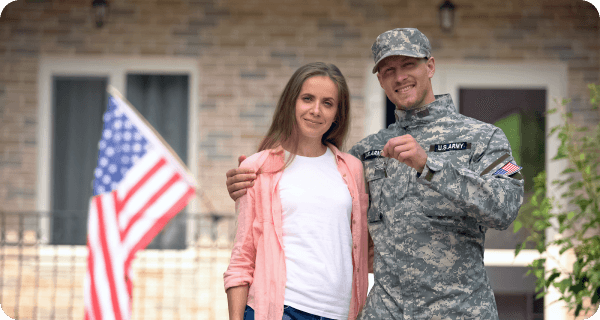 A military couple stands in front of their new home holding the keys to the house