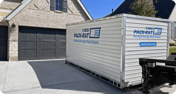 A 1-800-PACK-RAT portable storage container sits in front of a nice home's garage in the driveway