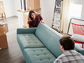 A couple begins to pick up and move a couch together as they move their belongings out of their old home