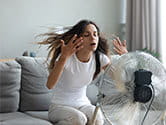 A woman sits in front of a fan to cool herself off