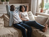 A happy couple sits on a couch in their home