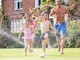 A happy family plays in the yard with a sprinkler