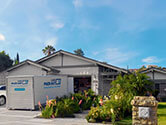 A 1-800-PACK-RAT portable storage container sits open in front of a home's open garage in the driveway on a bright sunny day