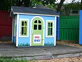 The children's playhouse 1-800-PACK-RAT made with Habitat for Humanity sitting in a garden at Passage Home.