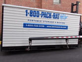 1-800-PACK-RAT Container lowered by truck in driveway.